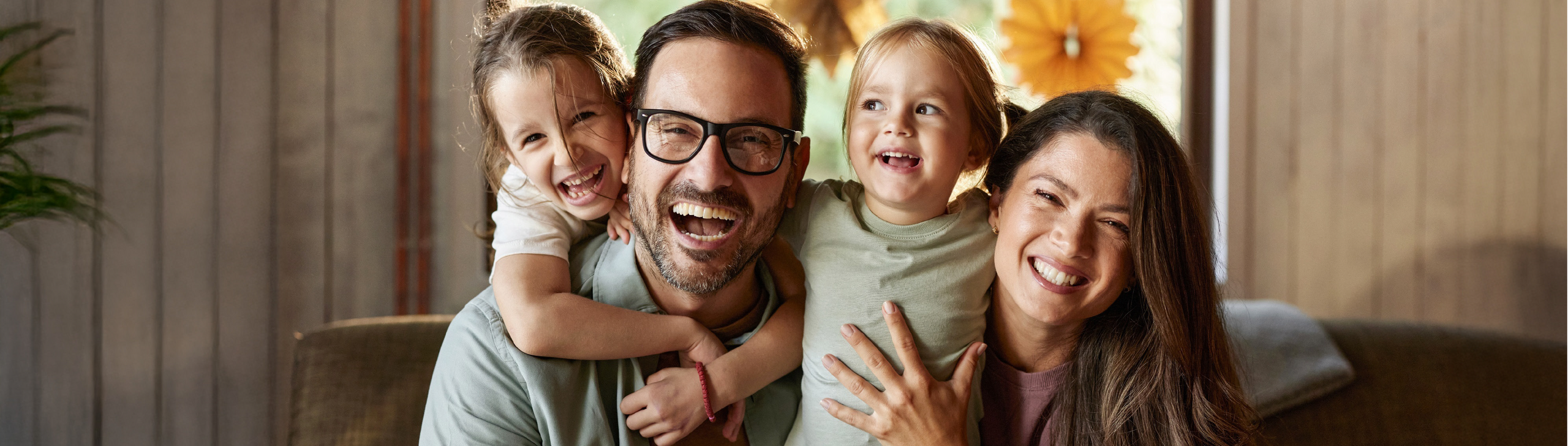 Glückliche Mutter, Vater und 2 Töchter sitzen auf dem Sofa und halten sich im Arm.