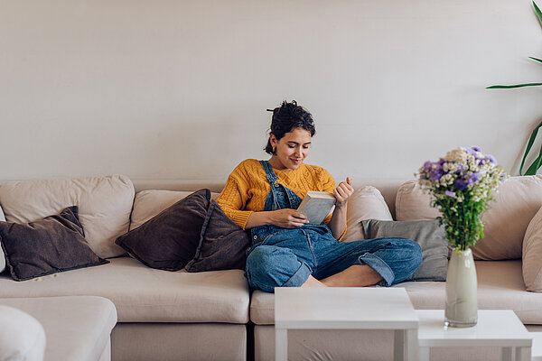 Frau sitzt auf ihrem Sofa und liest ein Buch.