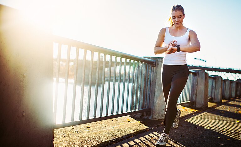 Junge sportliche Frau beim Joggen, schaut auf ihre Smartwatch.