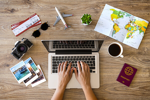 Draufsicht auf einen Laptop, um den Reiseunterlagen , Fotoapparat, Sonnenbrille und eine Tasse Kaffee stehen.