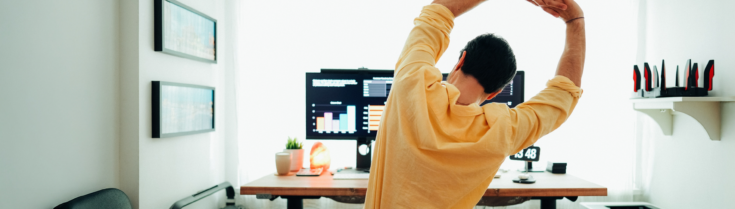 Mann steht vor seinem Schreibtisch und streckt seinen Rücken.