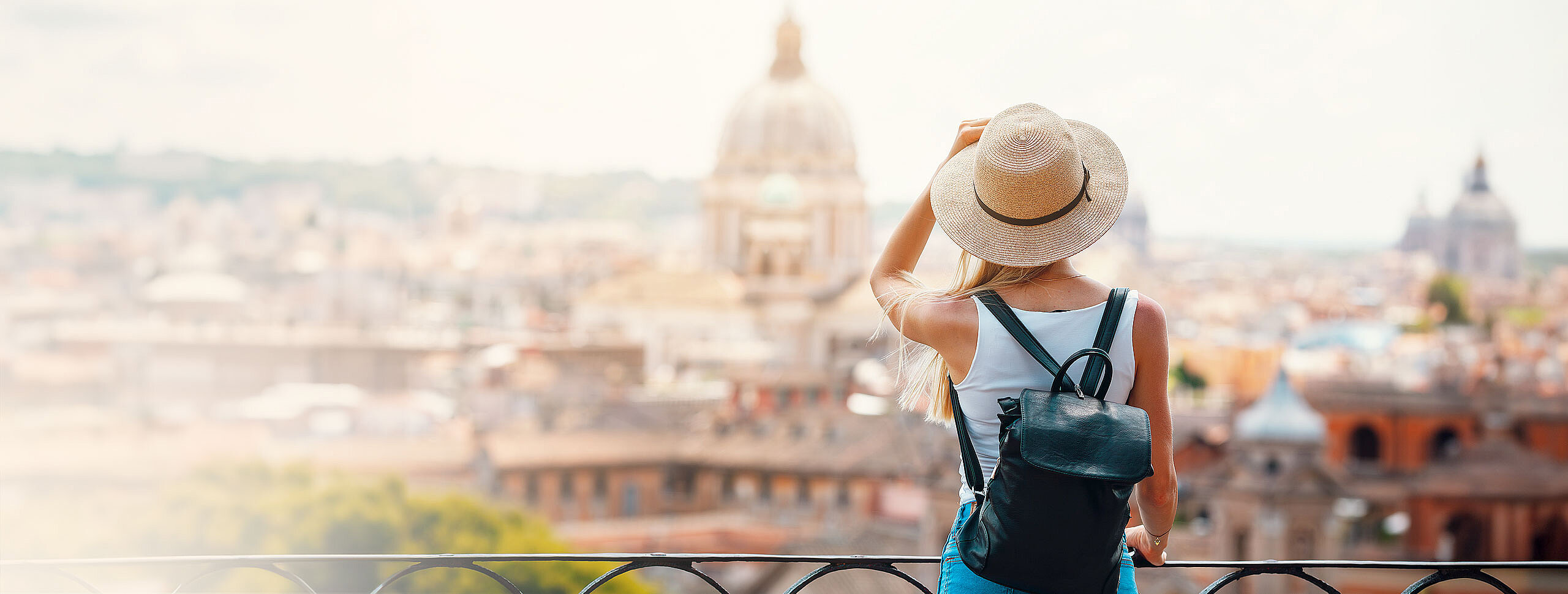 Touristin mit Sonnenhut und Rucksack geniest den Ausblick über eine Stadt.