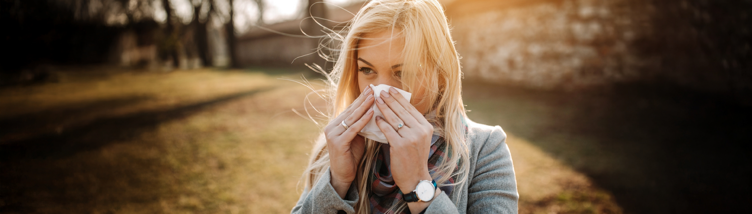 Frau mit Heuschnupfen putzt sich die Nase im Frien.