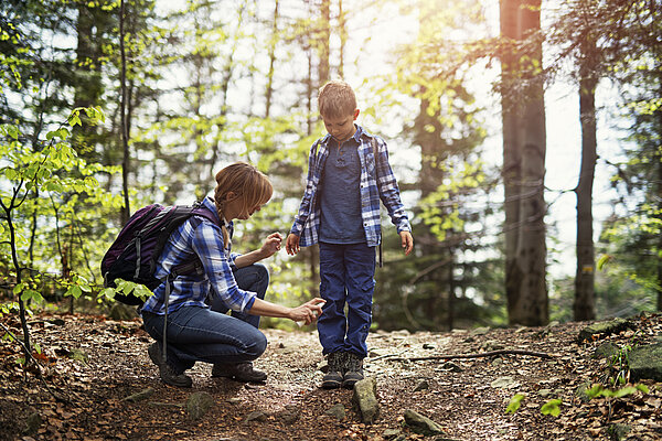Mutter und Sohn gehen im Wald spazieren. Die Mutter besprüht die Kleidung des Sohnes mit Zeckenschutz.