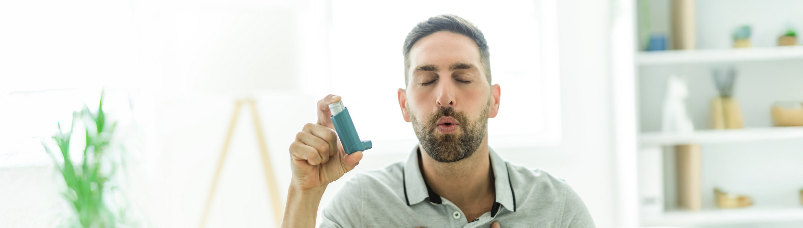 Junger Mann mit Asthma-Spray in der Hand atmet durch.