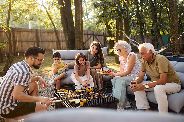 Eine Familie sitzt draußen im Garten und grillst gemeinsam. 