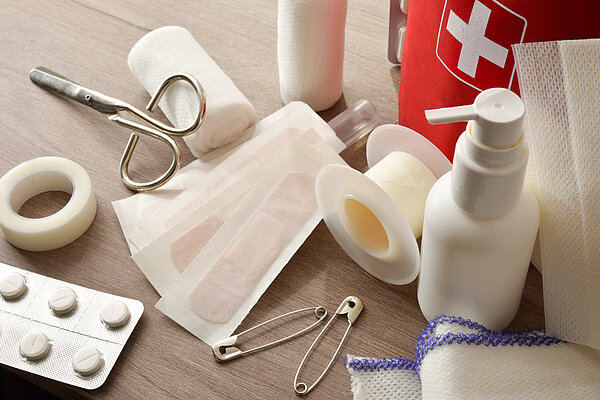 Verschiedene Verbandsmaterialien, Tabletten, Desinfektionsspray und weitere Inhalte einer Reiseapotheke.