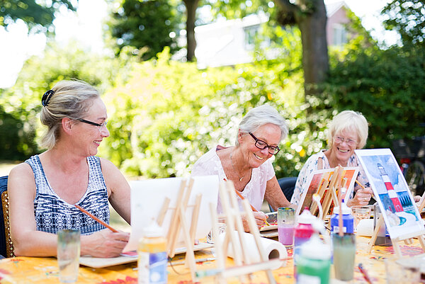 Ältere Frauen sitzen draußen an einem Tisch und malen