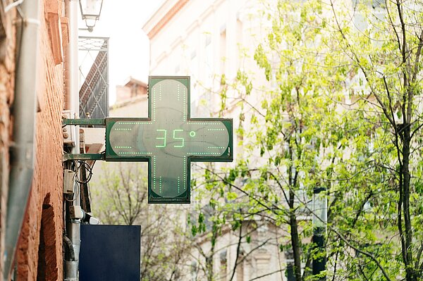Grünes Außenthermometer an Hauswand in Kreuzform. Es zeigt 35 Grad Celsius an.