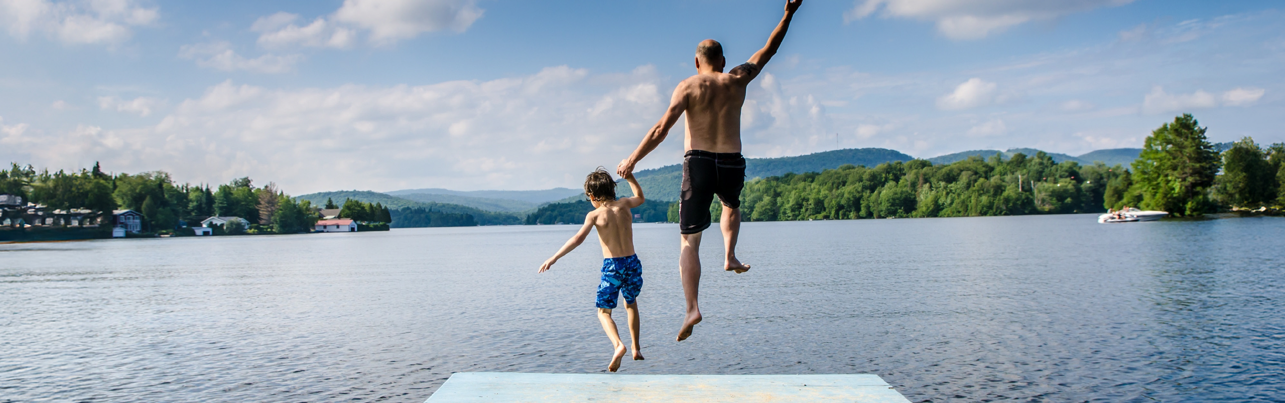 Vater und Sohn springen händehaltend von einem Steg ins Wasser.