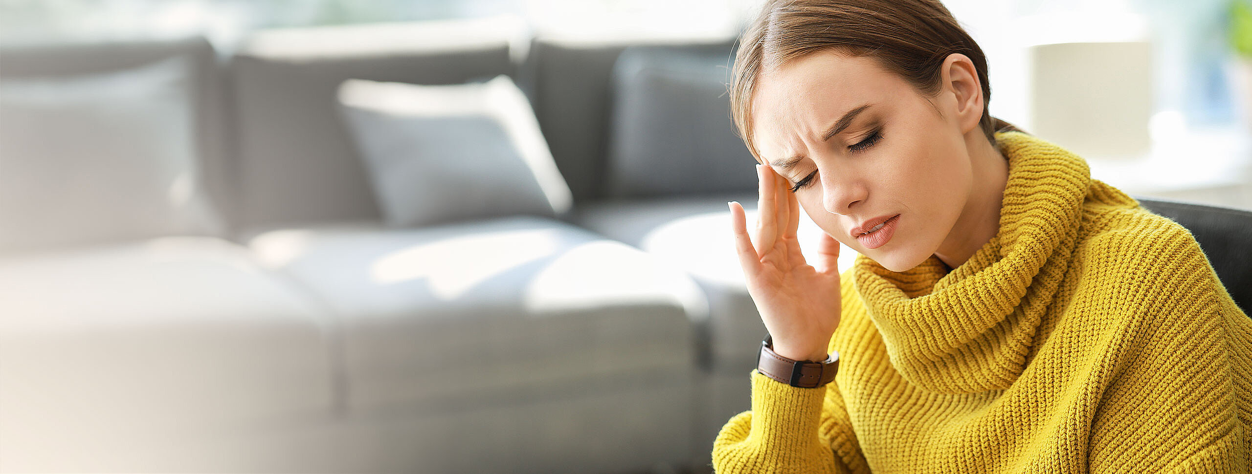 Frau hält sich den schmerzenden Kopf mit einer Hand.