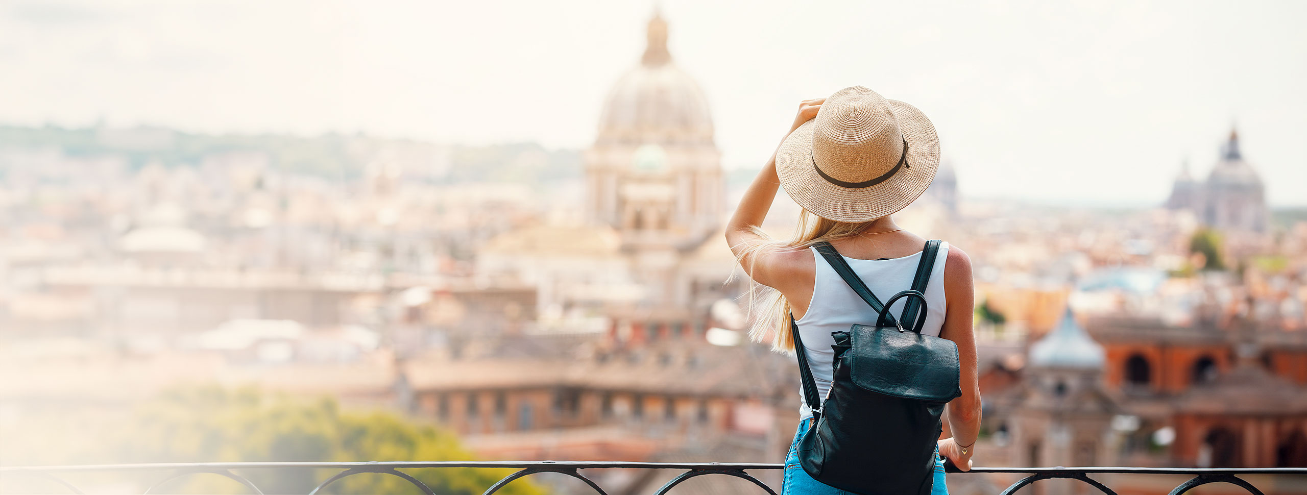 Touristin mit Sonnenhut und Rucksack geniest den Ausblick über eine Stadt.