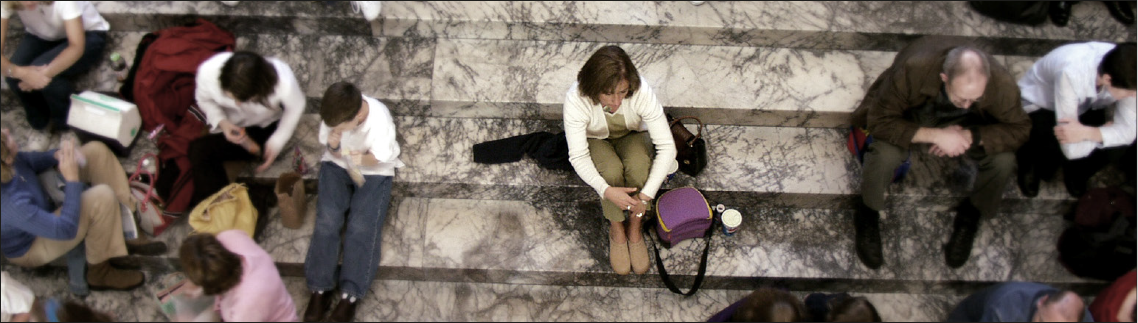 Frau sitzt allein auf einer Treppe umgeben von Menschen.