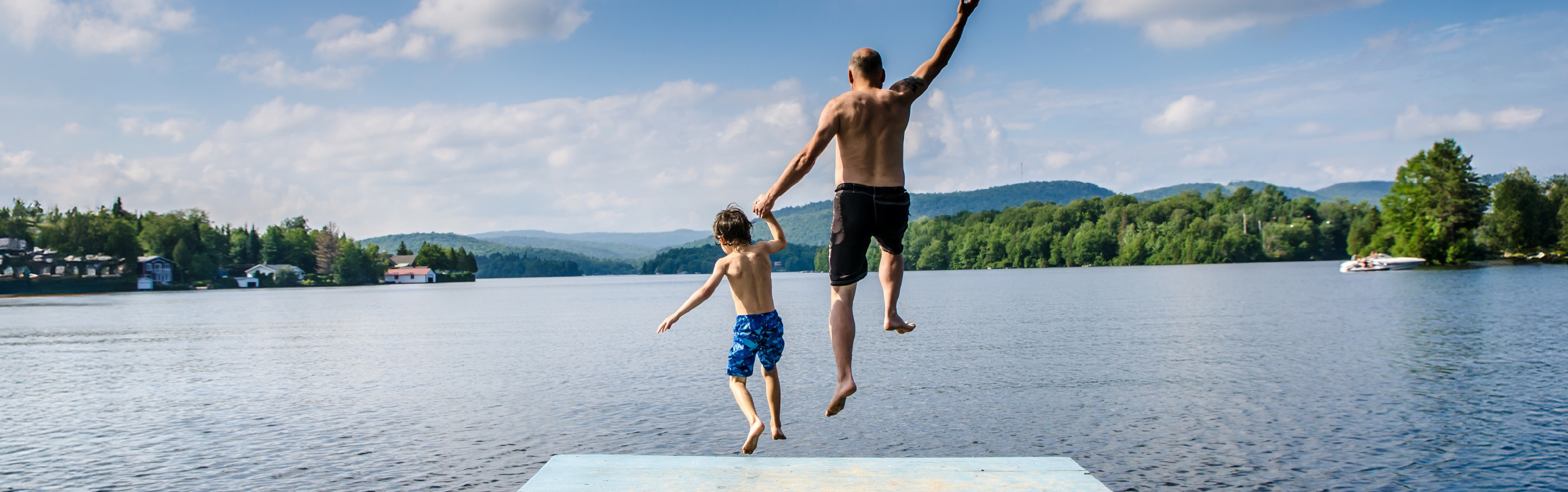 Vater und Sohn springen händehaltend von einem Steg ins Wasser.
