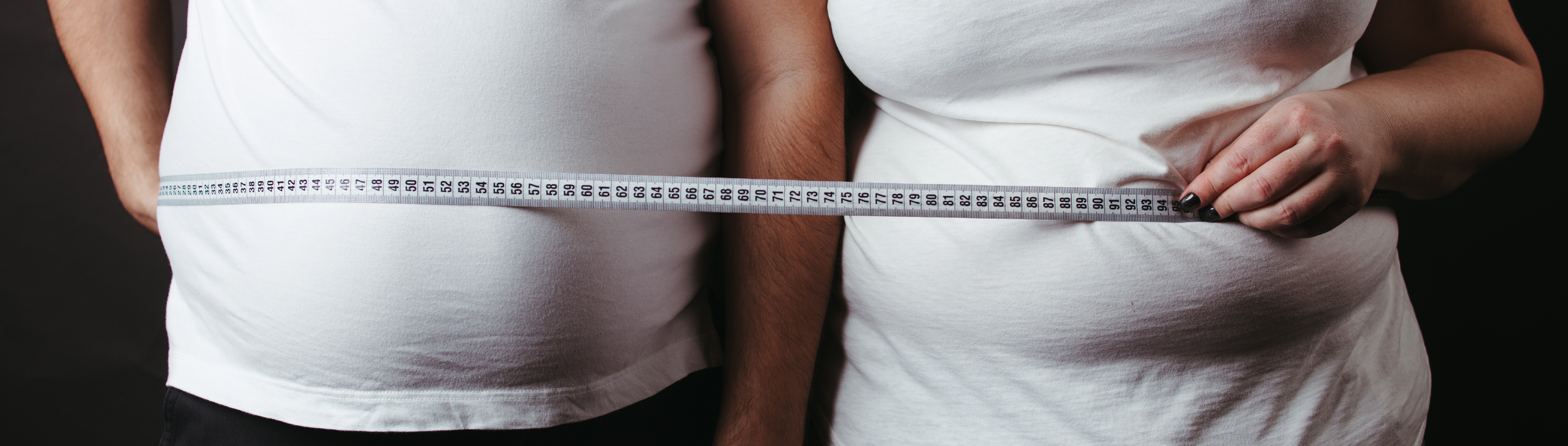 Oberkörper von korpulenterem Mann und Frau heben Maßband um sich.