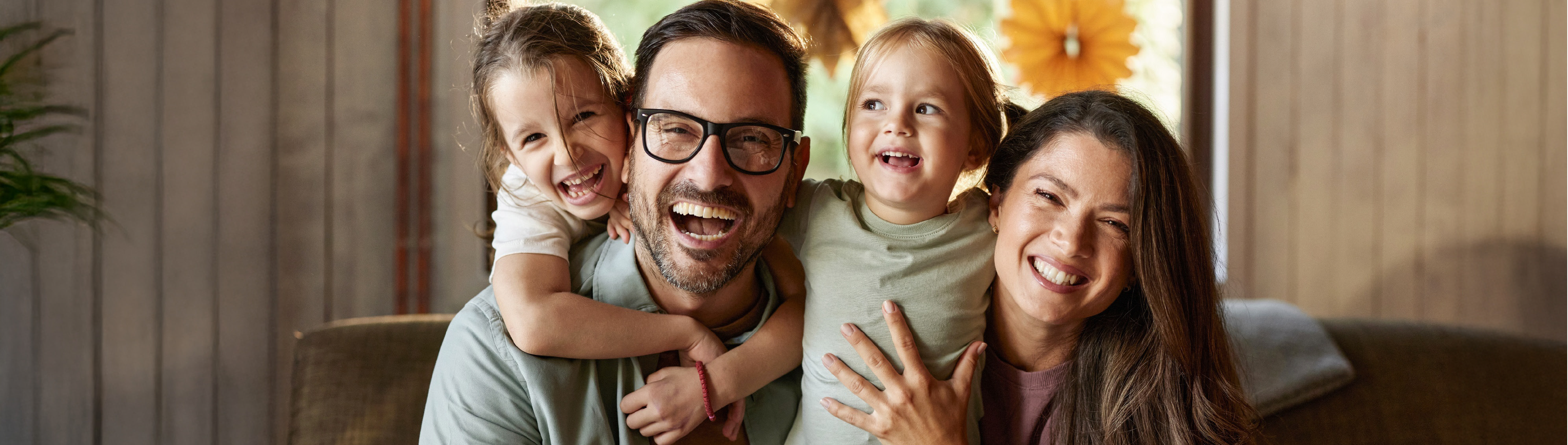 Glückliche Mutter, Vater und 2 Töchter sitzen auf dem Sofa und halten sich im Arm. 
