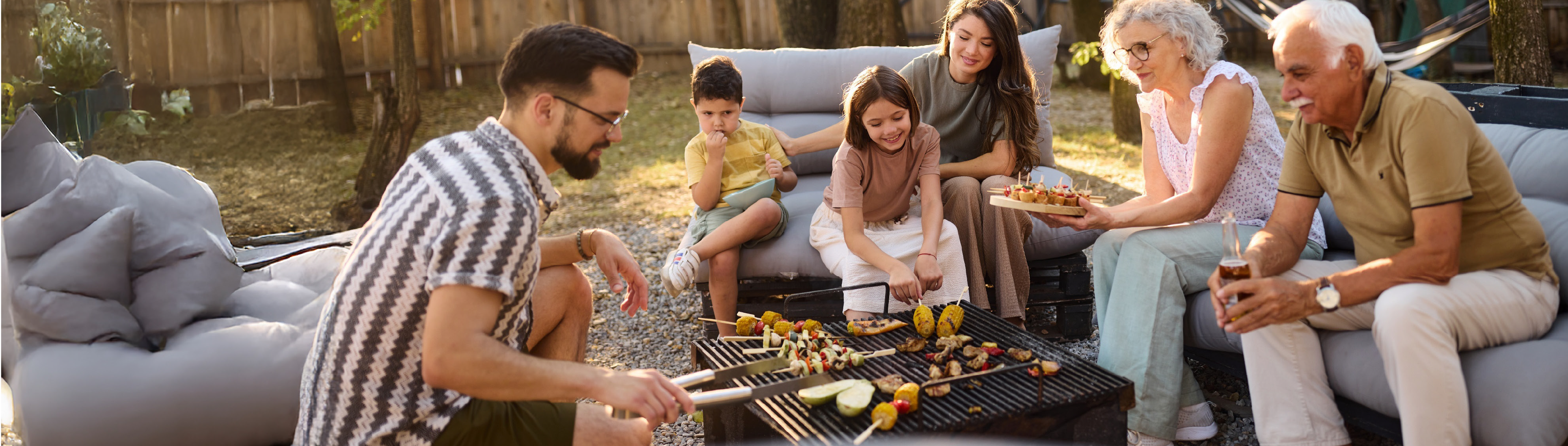 Eine Familie sitzt draußen im Garten und grillst gemeinsam. 
